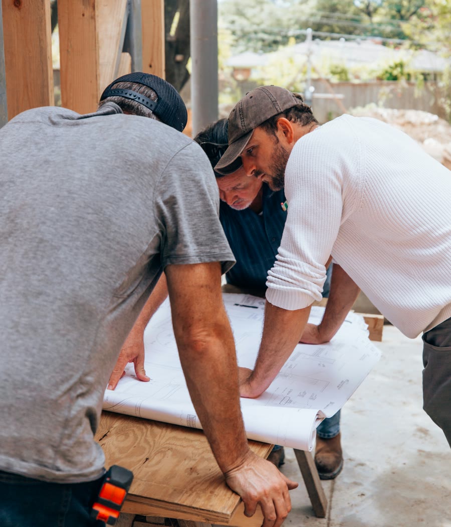 Tres constructores revisando los planos sobre un caballete en la obra